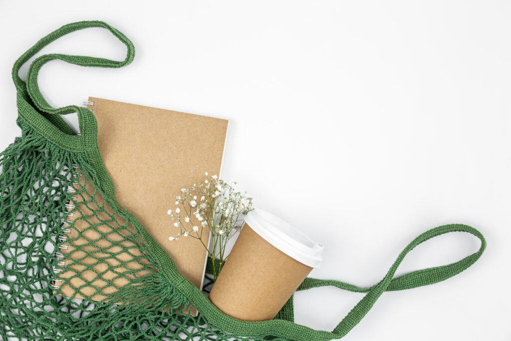 eco background with paper cup and recycled paper notepad in shopping bag.